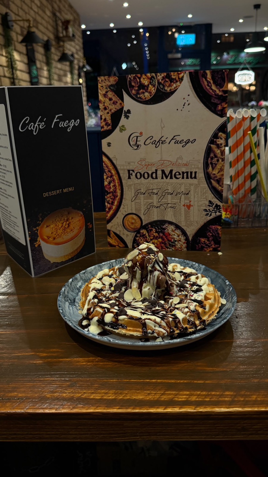 A chocolate-and-white-chocolate drizzled waffle dessert on a plate, with the Café Fuego food menu behind