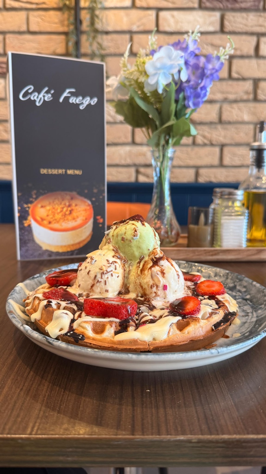 A loaded waffle with scoops of ice cream, strawberries and sauces, beside the Café Fuego dessert menu